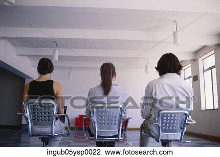 Stock Image - Rear view of two young women and a young man sitting on chairs. Fotosearch