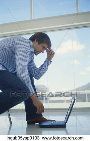 Stock Image - Side profile of a businessman working on a laptop on the floor. Fotosearch