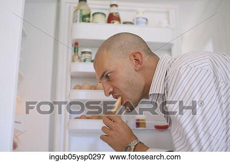 Side profile of a young man eating from a refrigerator View Large Photo Image Stock Photo - Side profile of a young man eating from a refrigerator. Fotosearch
