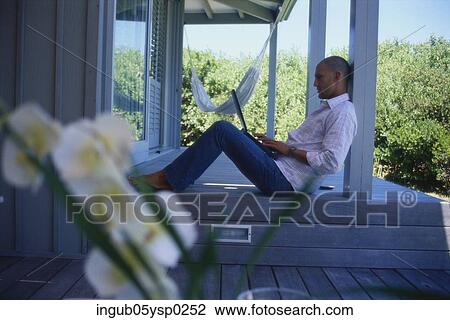 Stock Image - Side profile of a young man sitting on the floor and using a laptop. Fotosearch