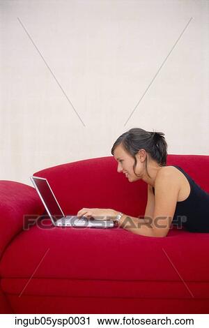 Side profile of a young woman lying on a couch and working on a laptop View Large Photo Image Stock Image - Side profile of a young woman lying on a couch and working on a laptop. Fotosearch
