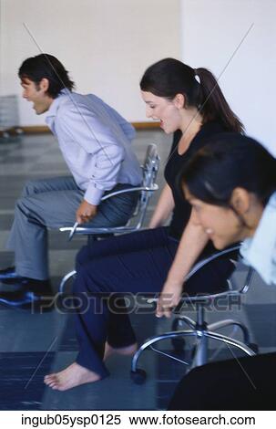 Stock Photography - Side profile of two young women and a young man sitting on chairs. Fotosearch