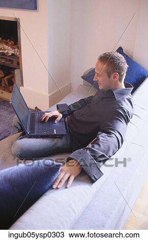 Side view of a young man sitting on a couch and using a laptop View Large Photo Image Stock Image - Side view of a young man sitting on a couch and using a laptop. Fotosearch