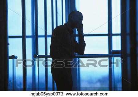 Stock Image - Silhouette of a young man standing near a window. Fotosearch