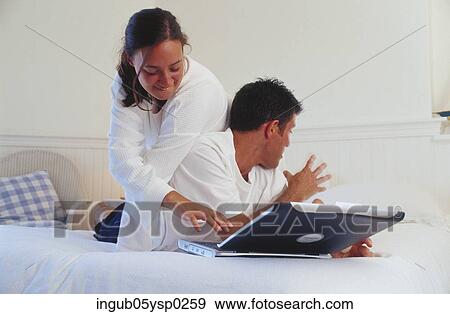 Young couple lying on a bed with a laptop View Large Photo Image Stock Photo - Young couple lying on a bed with a laptop. Fotosearch