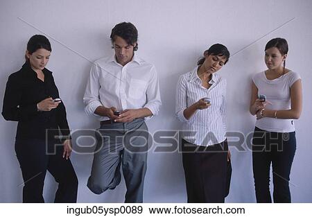 Stock Photo - Young man and three young women leaning on a wall with mobile phones. Fotosearch