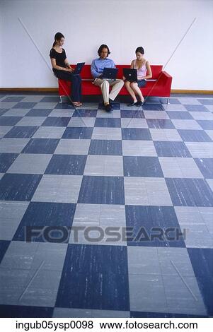 Stock Photo - Young man and two young women sitting on a couch and working on laptops. Fotosearch