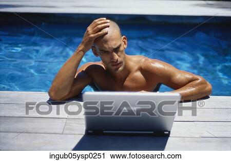 Stock Image - Young man in a swimming pool using a laptop. Fotosearch