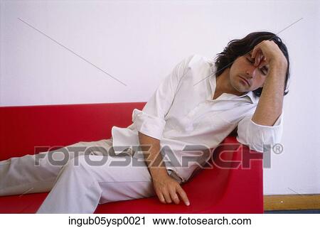 Stock Image - Young man reclining on a couch with his hand on his head. Fotosearch