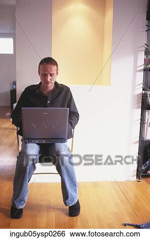 Stock Photograph - Young man sitting on a chair with a laptop. Fotosearch