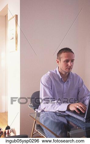 Stock Photograph - Young man sitting on a chair with a laptop. Fotosearch