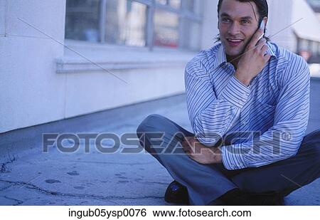 Stock Photograph - Young man sitting on the floor and talking on a mobile phone. Fotosearch