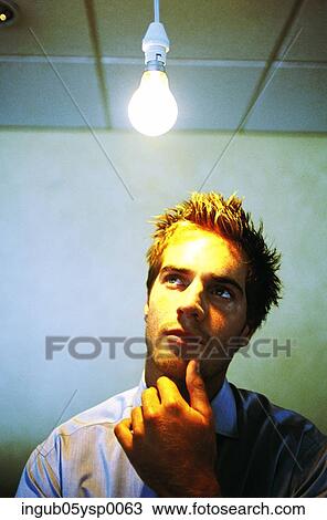 Stock Image - Young man standing under a light bulb and looking up. Fotosearch