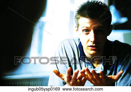 Stock Photo - Young man talking to a person sitting across him. Fotosearch