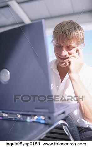 Stock Photo - Young man using a laptop and a mobile phone. Fotosearch