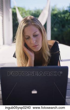 Stock Image - Young woman lying down and using a laptop. Fotosearch
