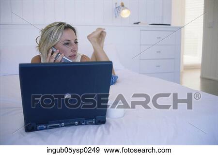 Stock Photo - Young woman lying on a bed and using a laptop. Fotosearch