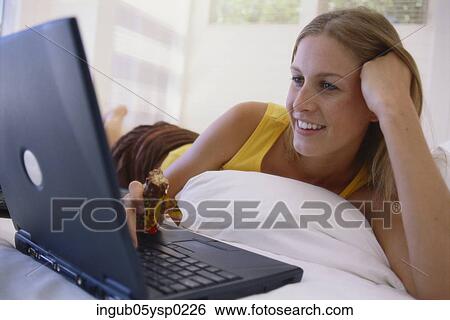 Young woman lying on a bed and working on a laptop View Large Photo Image Stock Photograph - Young woman lying on a bed and working on a laptop. Fotosearch
