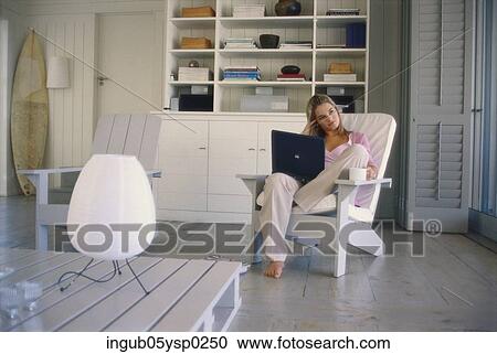 Young woman sitting on a chair with a laptop View Large Photo Image Stock Image - Young woman sitting on a chair with a laptop. Fotosearch