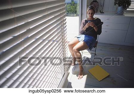 Young woman sitting on a chair with a mobile phone View Large Photo Image Stock Photograph - Young woman sitting on a chair with a mobile phone. Fotosearch