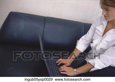 Stock Photo - Young woman sitting on a couch using a laptop. Fotosearch