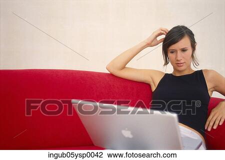 Young woman sitting on a couch with a laptop View Large Photo Image Stock Image - Young woman sitting on a couch with a laptop. Fotosearch
