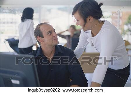 Stock Image - Young woman talking to a young man in an office. Fotosearch