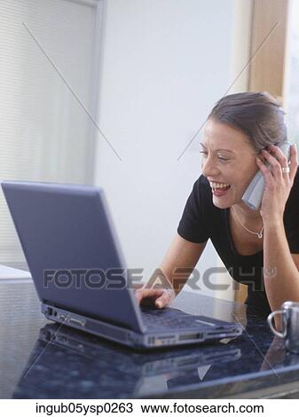 Young woman using a laptop and a mobile phone View Large Photo Image Stock Image - Young woman using a laptop and a mobile phone. Fotosearch