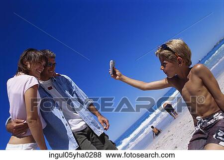 Stock Photo - Boy taking a photograph of a mid adult couple. Fotosearch