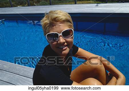 Stock Photo - Close-up of a young woman sitting beside a swimming pool. Fotosearch