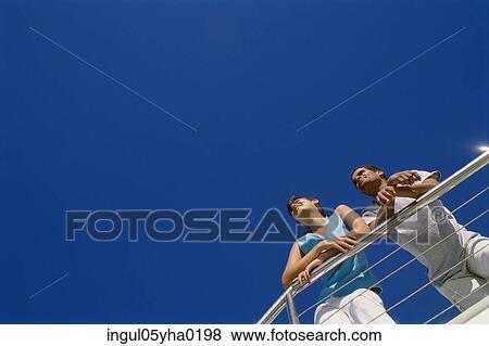 Low angle view of a young couple standing against a railing View Large Photo Image Stock Photo - Low angle view of a young couple standing against a railing. Fotosearch