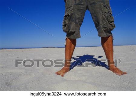 Picture - Low section view of a man standing on the sand on the beach. Fotosearch