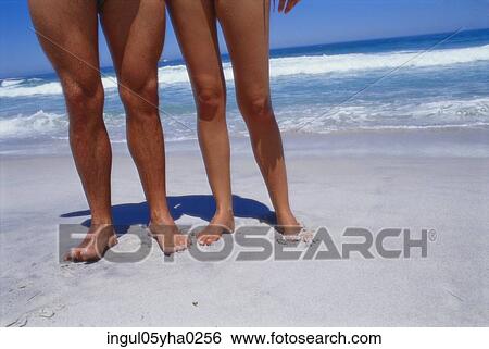 Stock Photograph - Low section view of two people standing on the beach. Fotosearch
