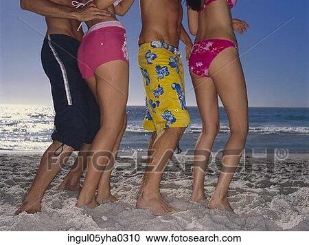 Stock Image - Low section view of two young couples standing on the beach. Fotosearch