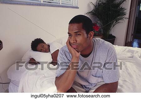 Mid adult man sitting on a bed with a mid adult woman lying down behind him View Large Photo Image Stock Photo - Mid adult man sitting on a bed with a mid adult woman lying down behind him. Fotosearch