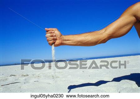 Stock Image - Person pouring sand on the beach. Fotosearch