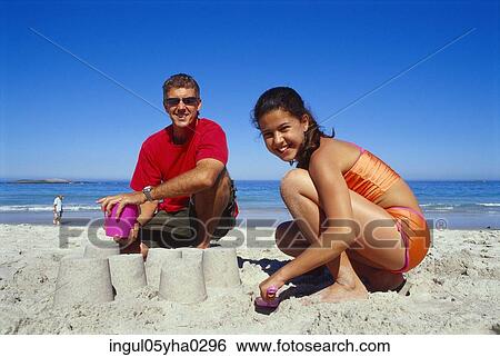 Stock Photograph - Portrait of a father and his daughter making sand castles on the beach. Fotosearch