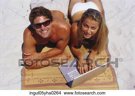 Picture - Portrait of a young couple working on a laptop on the beach. Fotosearch