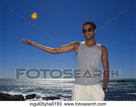 Stock Image - Portrait of a young man throwing a ball in the air. Fotosearch