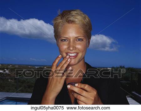 Portrait of a young woman applying lipstick View Large Photo Image Stock Photography - Portrait of a young woman applying lipstick. Fotosearch