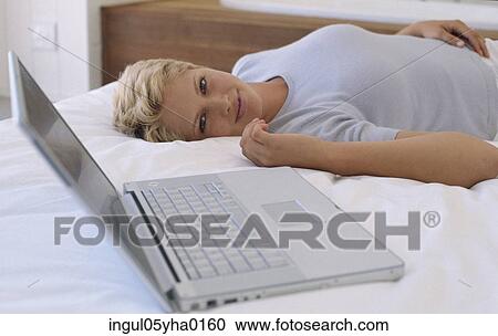 Portrait of a young woman lying on a bed beside a laptop View Large Photo Image Stock Image - Portrait of a young woman lying on a bed beside a laptop. Fotosearch