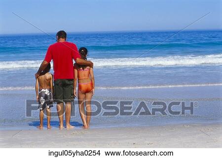 Rear view of a father standing with his son and daughter on the beach View Large Photo Image Picture - Rear view of a father standing with his son and daughter on the beach. Fotosearch