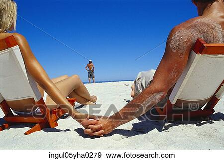 Stock Photo - Rear view of a young couple sitting on chairs on the beach. Fotosearch