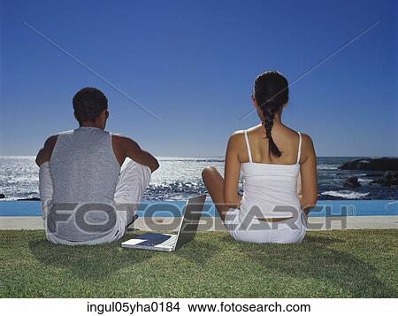 Rear view of a young couple sitting beside a swimming pool View Large Photo Image Picture - Rear view of a young couple sitting beside a swimming pool. Fotosearch