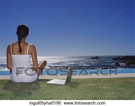 Stock Image - Rear view of a young woman sitting on a lawn. Fotosearch
