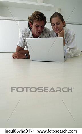 Stock Image - Young couple lying on the floor in front of a laptop. Fotosearch