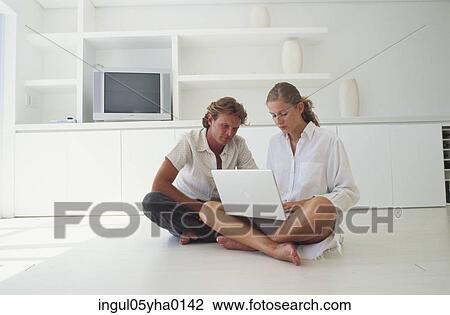 Stock Image - Young couple sitting on the floor with a laptop. Fotosearch