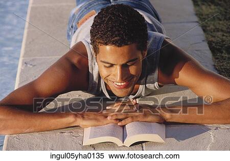 Young man lying down reading a book View Large Photo Image Stock Photography - Young man lying down reading a book. Fotosearch