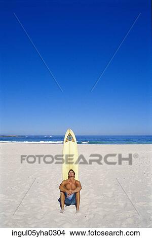 Young man sitting on the beach in front of a surfboard View Large Photo Image Picture - Young man sitting on the beach in front of a surfboard. Fotosearch