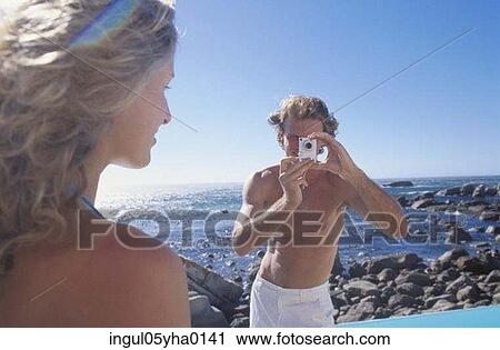 Stock Image - Young man taking a photograph of a young woman. Fotosearch
